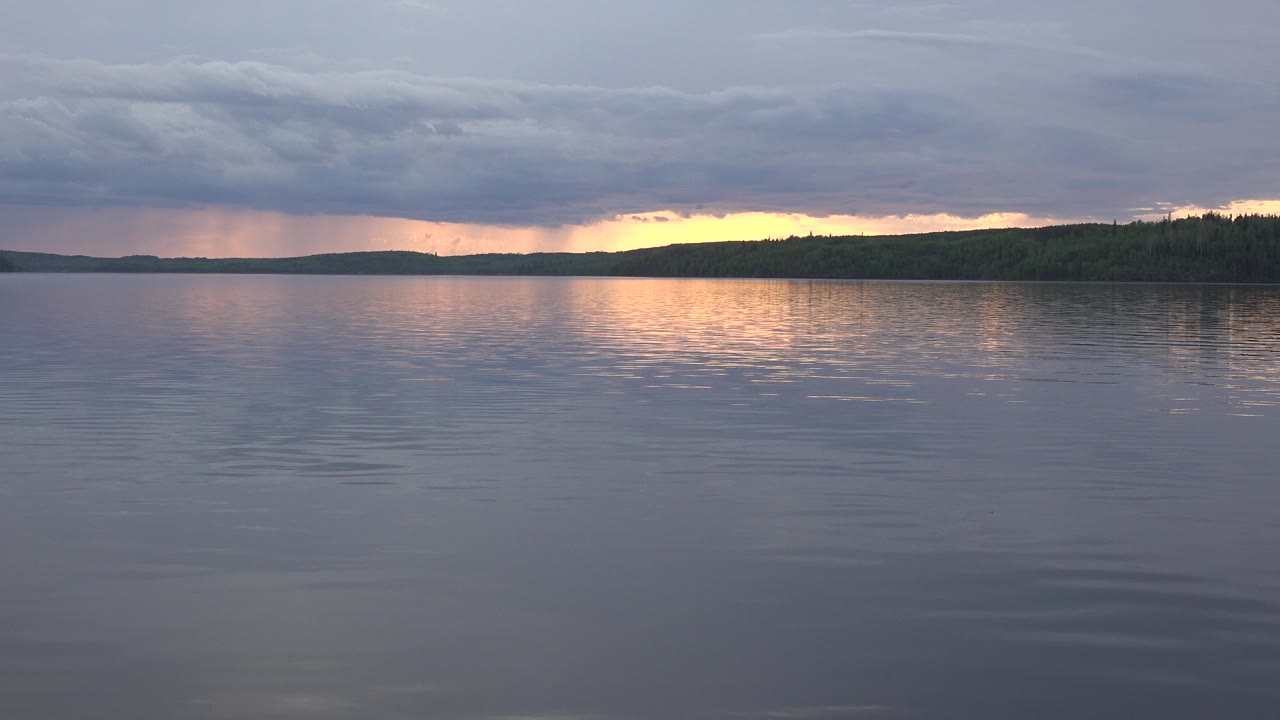 Red Lake, Canada at 0:01 shows calm foreground water, a dark forested horizon, a bright orange-yellow break in the clouds, and no visible people.