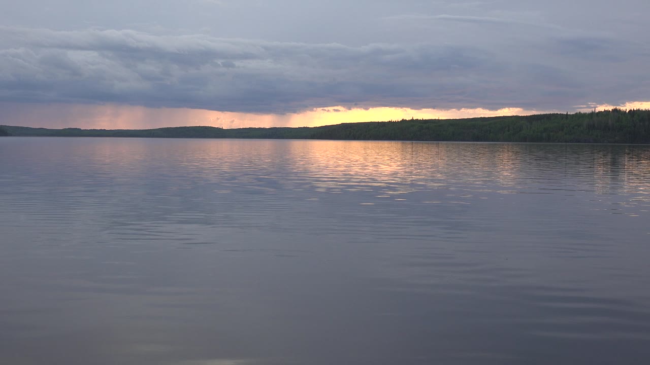 Open lake with low wooded shoreline and storm clouds at sunset