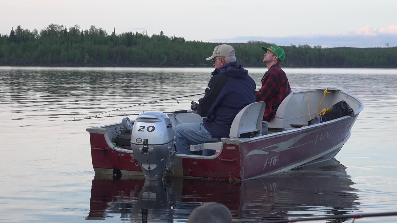 Two people fishing from a red motorboat on a calm lake.