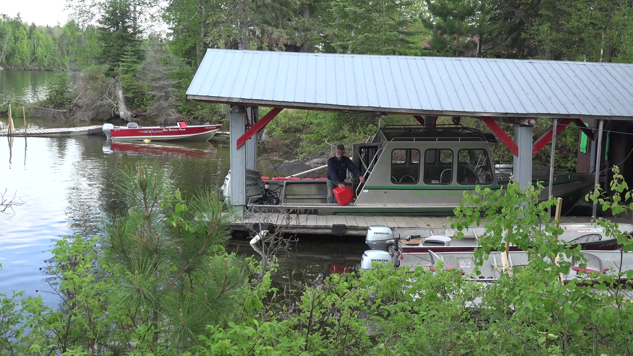 Covered lakeside dock with boats and a person near a red container.