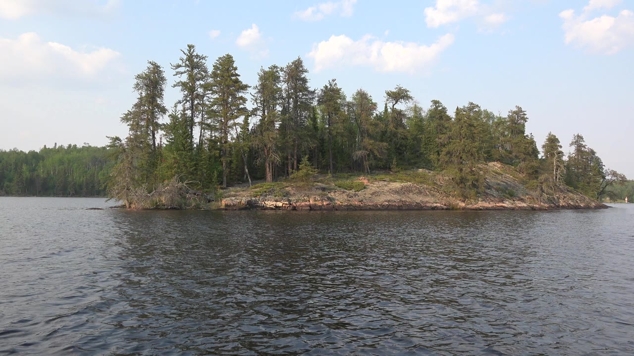 Opening frame of Red Lake, Canada showing choppy dark water in the foreground, a rocky island covered with trees across the center, distant shoreline trees, and no visible people.