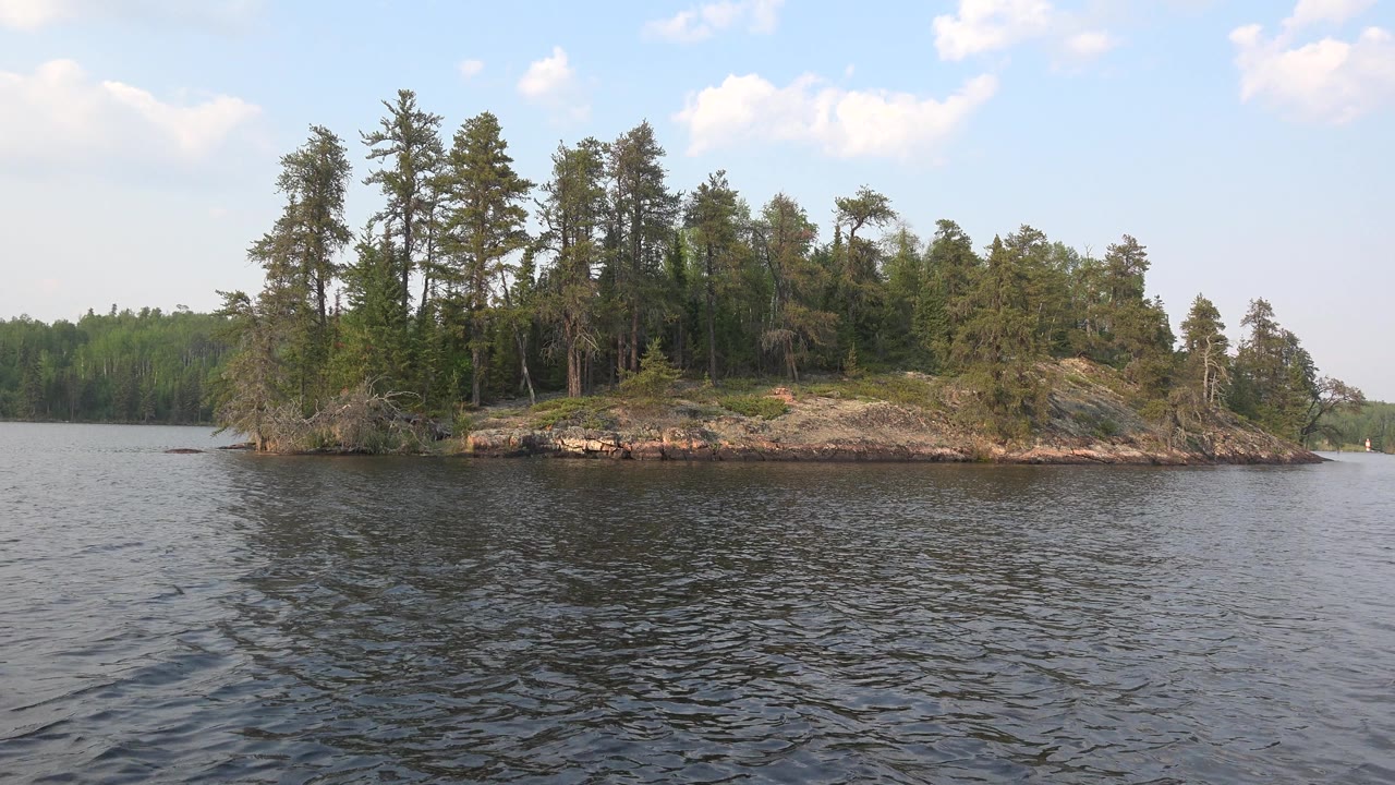 Rocky wooded island with choppy water and a distant tree line.