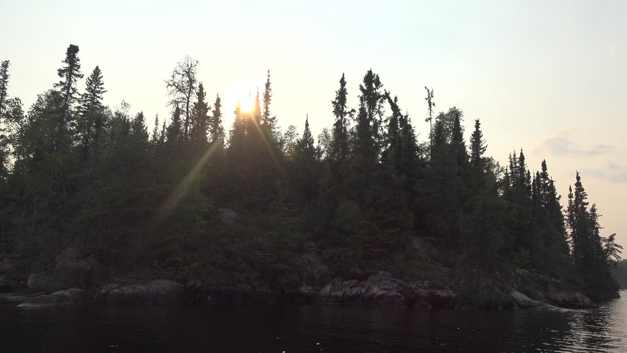 Forested island shoreline with low sun over calm water.