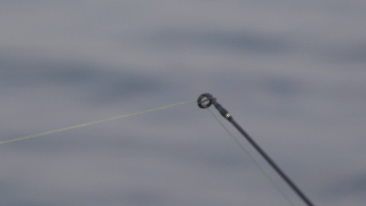 Fishing rod tip and pale line over gray rippled water.