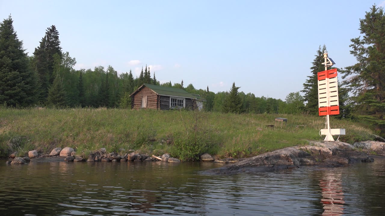 Red and white shoreline marker beside trees and cabin