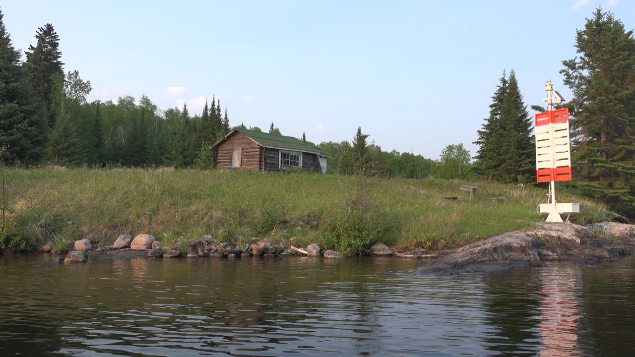 Cabin and red and white marker on a tree-lined lake shore.