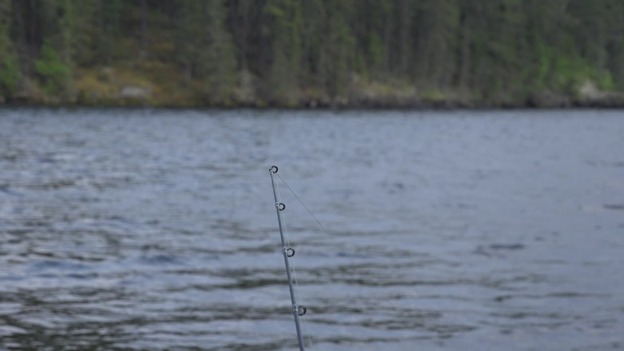 Angled fishing rod tip in front of choppy lake water.