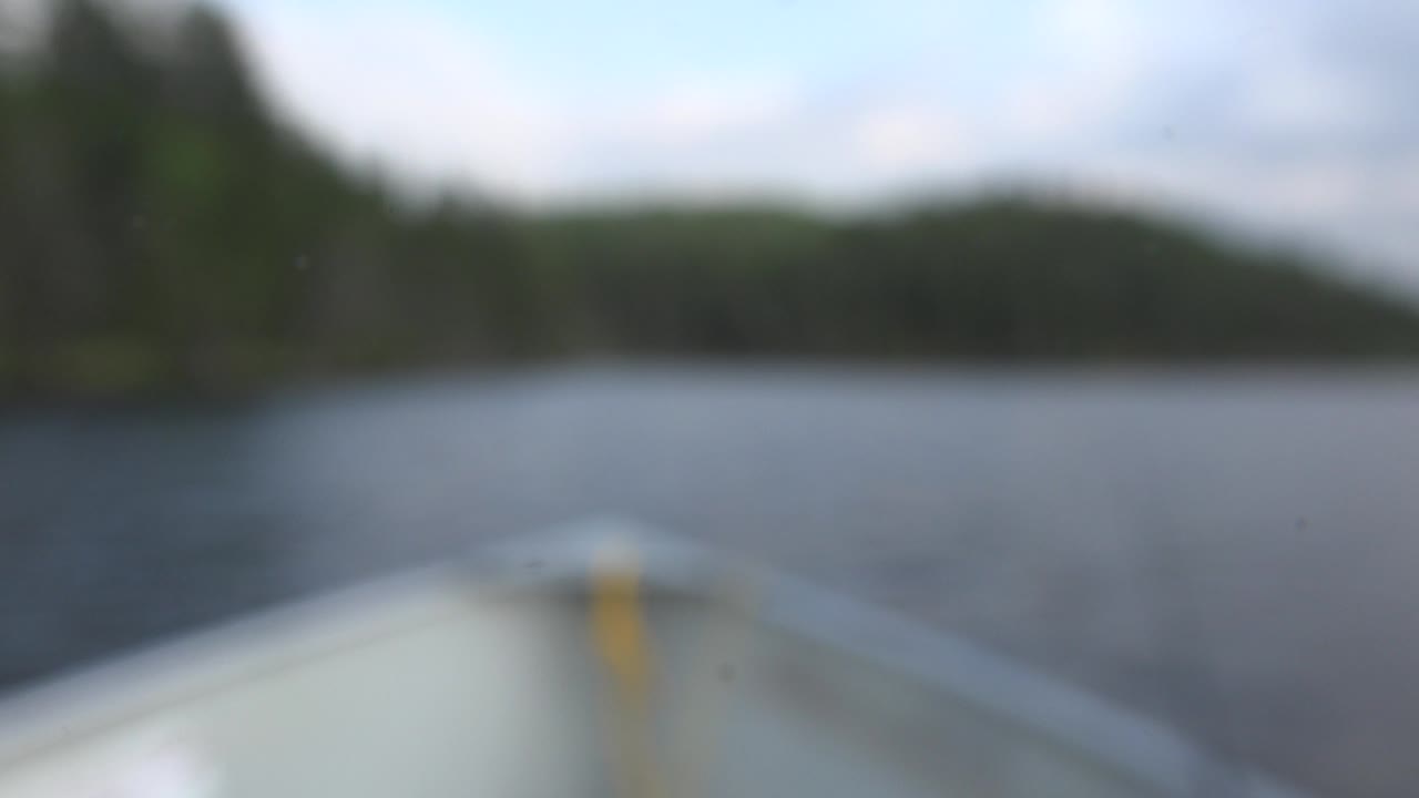 Out-of-focus opening frame from Red Lake, Canada, with a pale boat bow at the bottom, dark lake water ahead, a soft tree line in the distance, and no visible people.