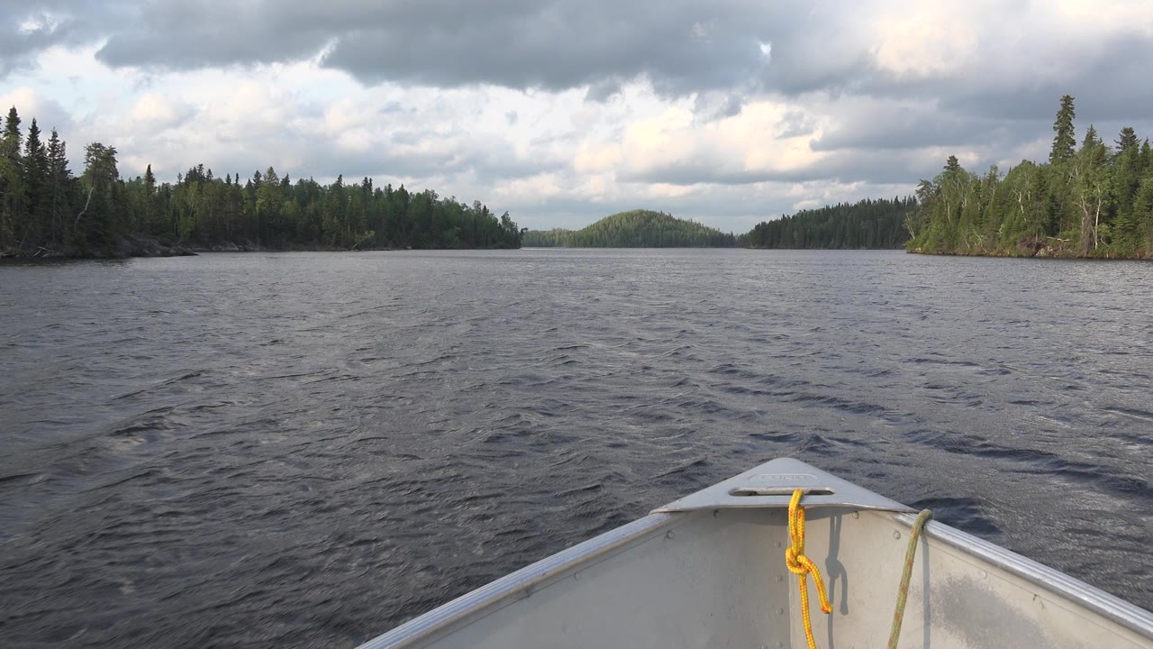 A small white boat bow points across rippled Red Lake water toward forested shorelines and low hills under gray clouds, with no visible people.