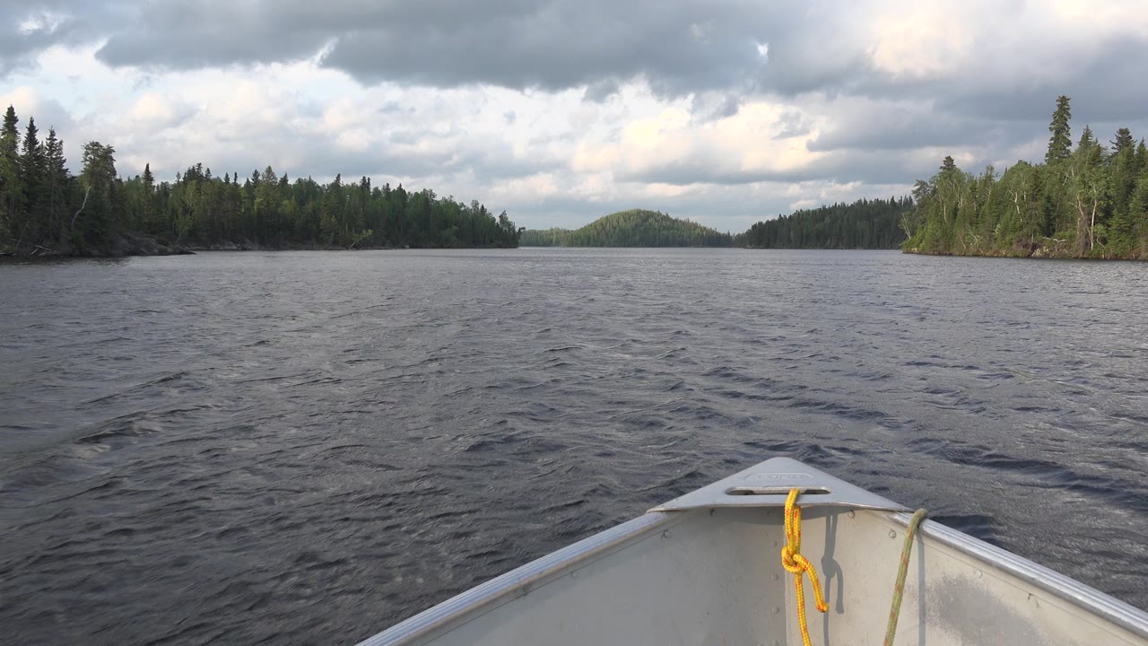 The centered boat bow and yellow rope face slightly darker ripples on Red Lake, with evergreen shoreline spreading across the horizon and no visible people.