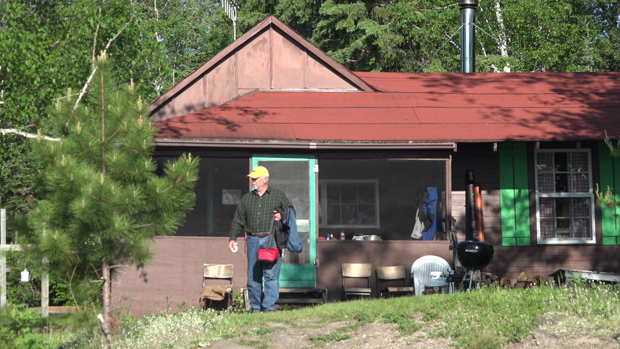 Man steps away from a green cabin door carrying a red bag.