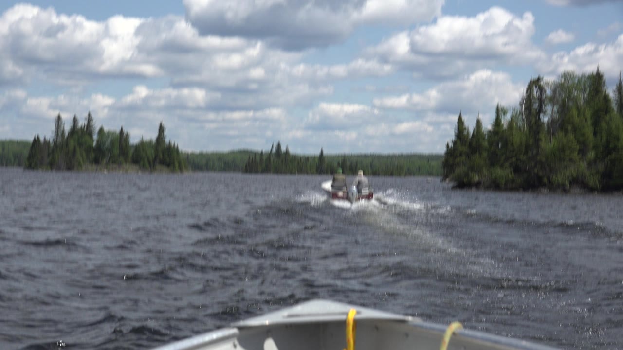 Small motorboat ahead on choppy lake water with forested shore and boat bow foreground.