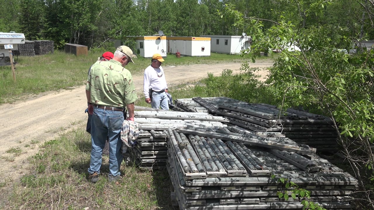 Three men stand around metal stacks with brush and trailers in the background.