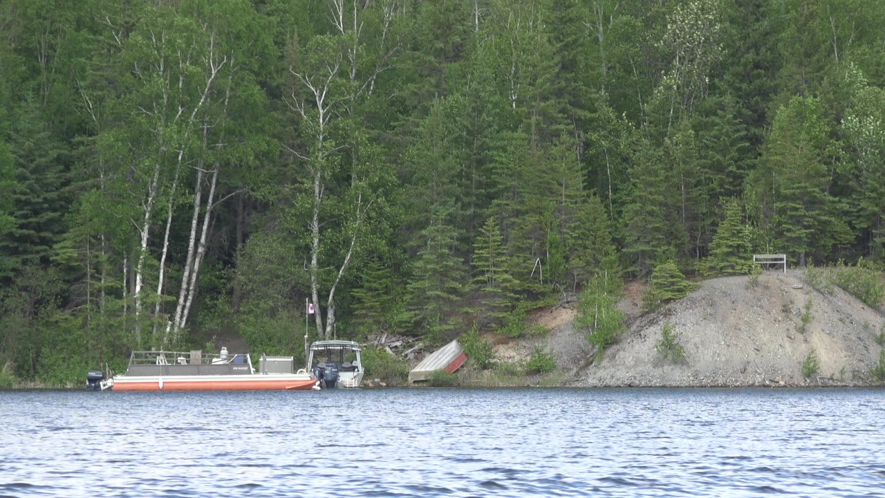 At Red Lake, Canada, a small orange-and-white boat sits near a forested shore with rippled water in front, exposed pale rock behind it, and no visible people.