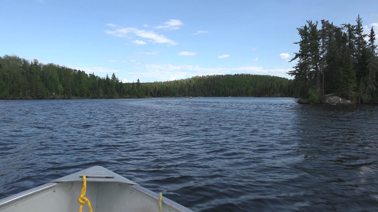 Boat bow crossing open blue water with forest banks on both sides.