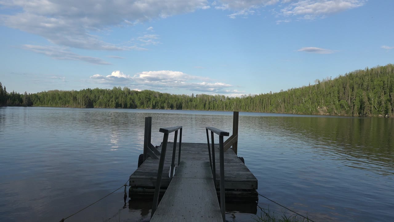 Wooden pier on calm water with forested shoreline across the lake.