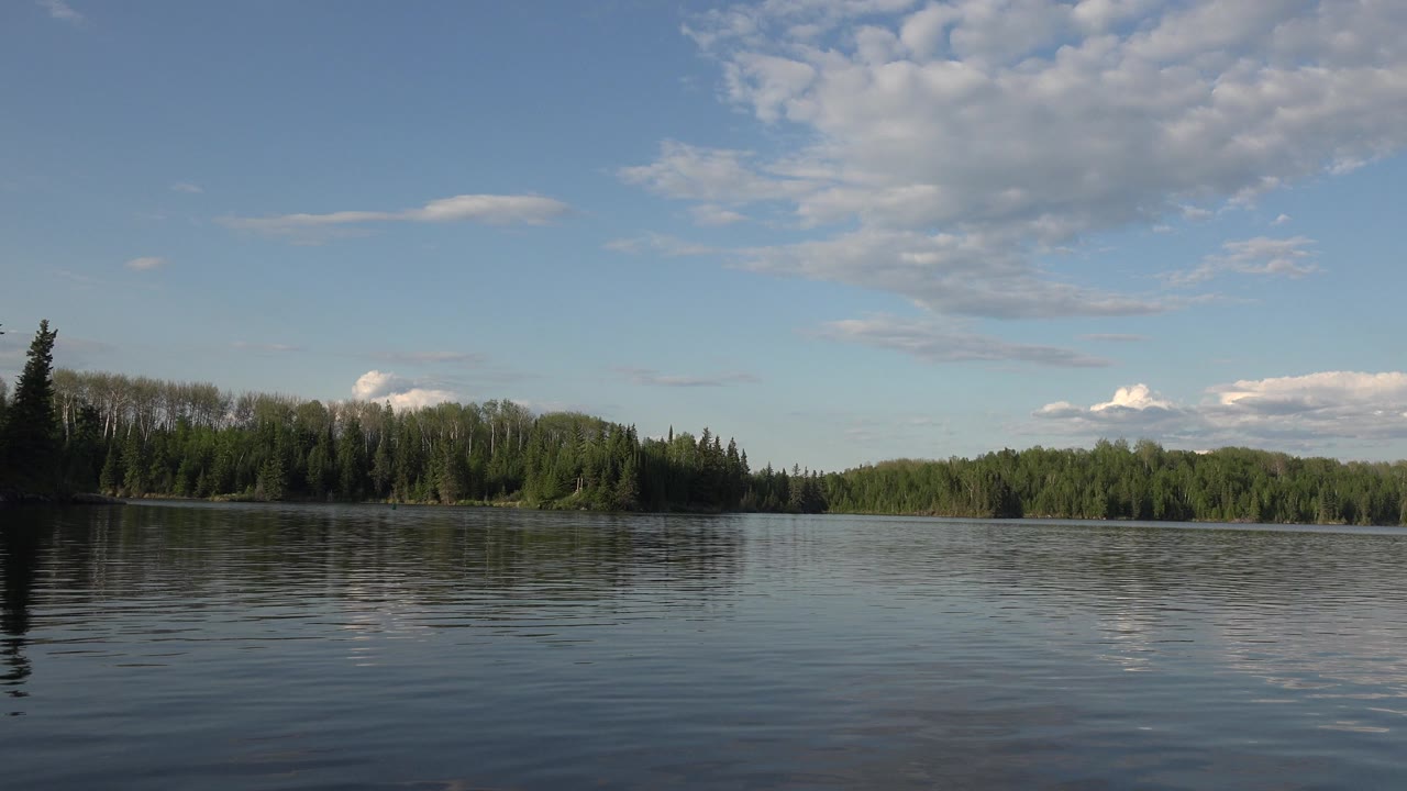 A broad Red Lake, Canada water view shows darker ripples in front, reflected cloud shapes on the lake, a low forested horizon, and no visible people.