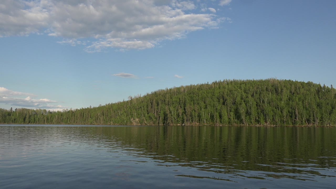Wide lake view with a forested hill and clouded blue sky.