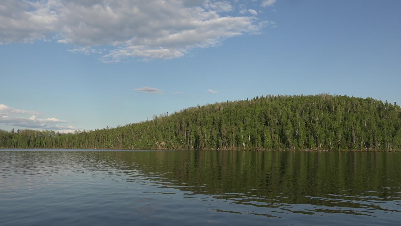 At Red Lake, Canada, the green hill sits slightly right of center with its dark reflection broken by small ripples, and no visible people appear.