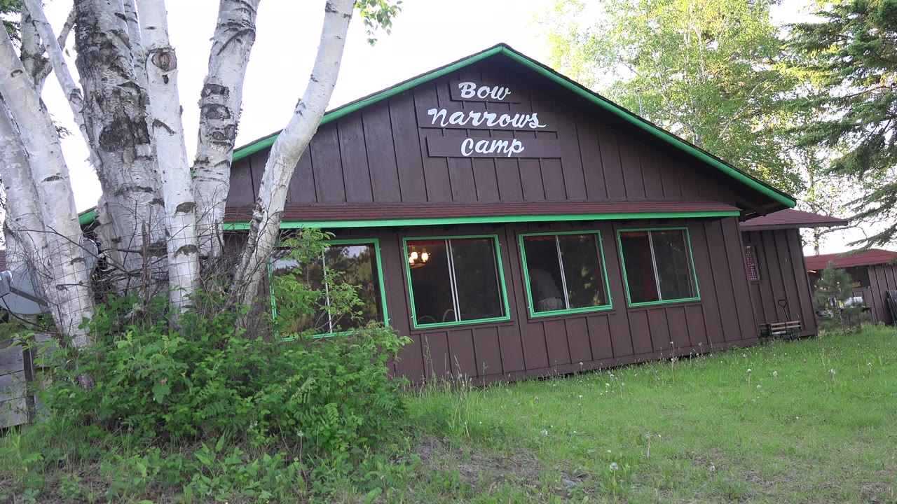 Brown wooden camp building with green trim behind birch trees