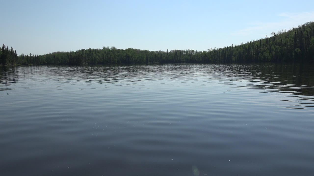 Opening frame of Red Lake, Canada with rippled blue water in the foreground, a dark green treeline across the horizon, pale sky above, and no visible people.