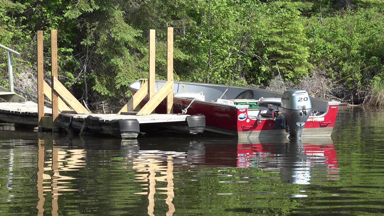 Red boat with outboard motor beside dock and green shoreline.