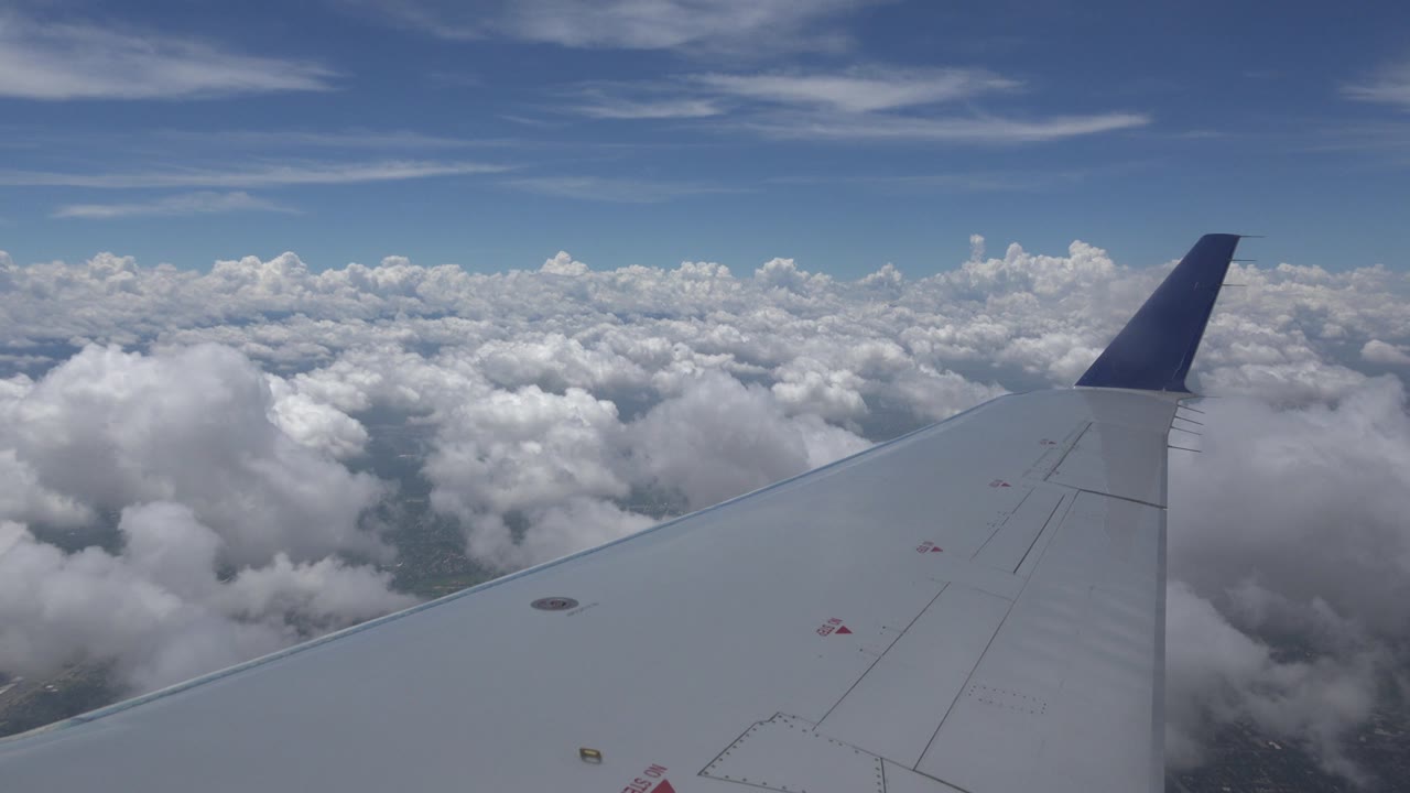 Blue-tipped airplane wing over scattered cloud banks