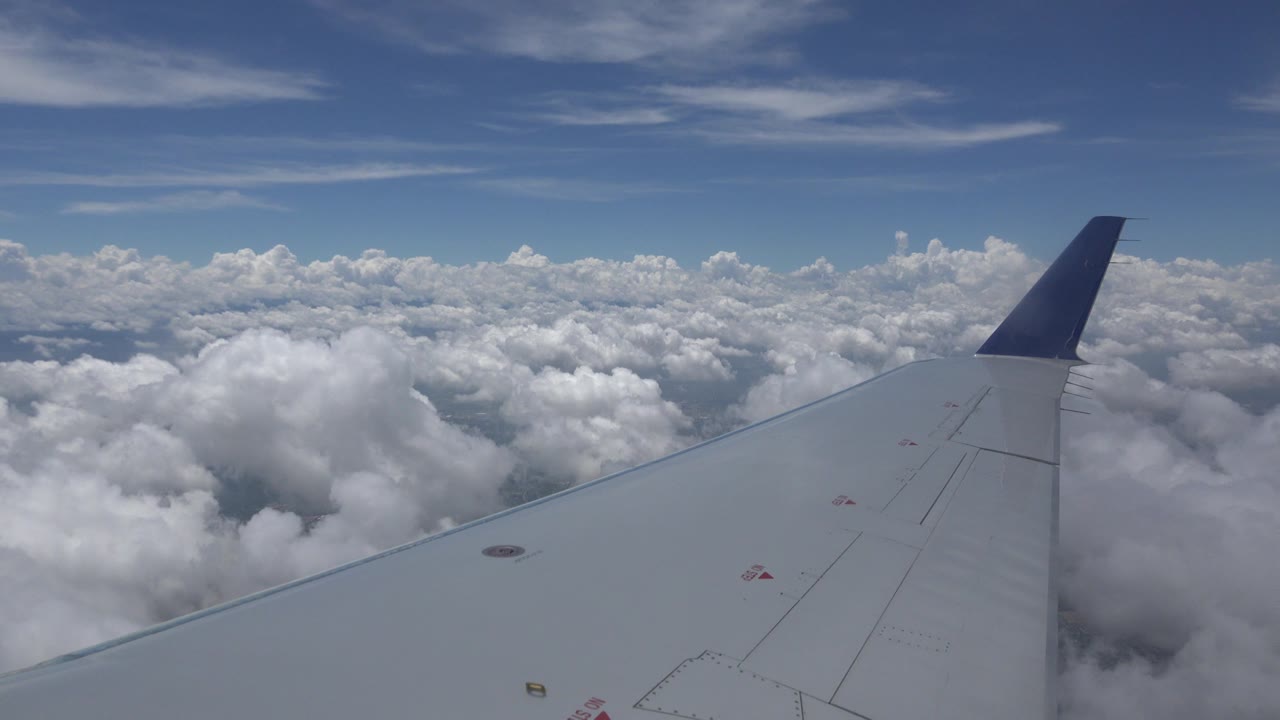 Airplane wing seen from a window over layered clouds near Winnipeg Canada, with blue sky above and no visible people.