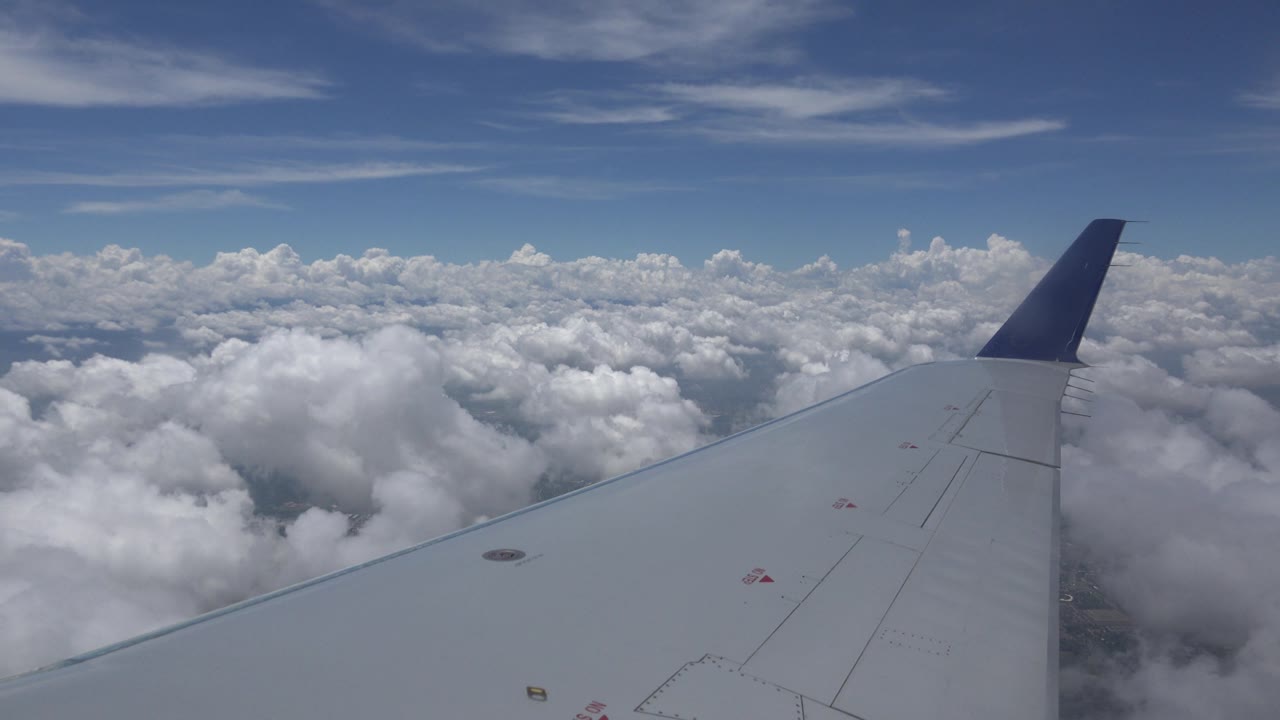 Airplane wingtip above bright cloud tops
