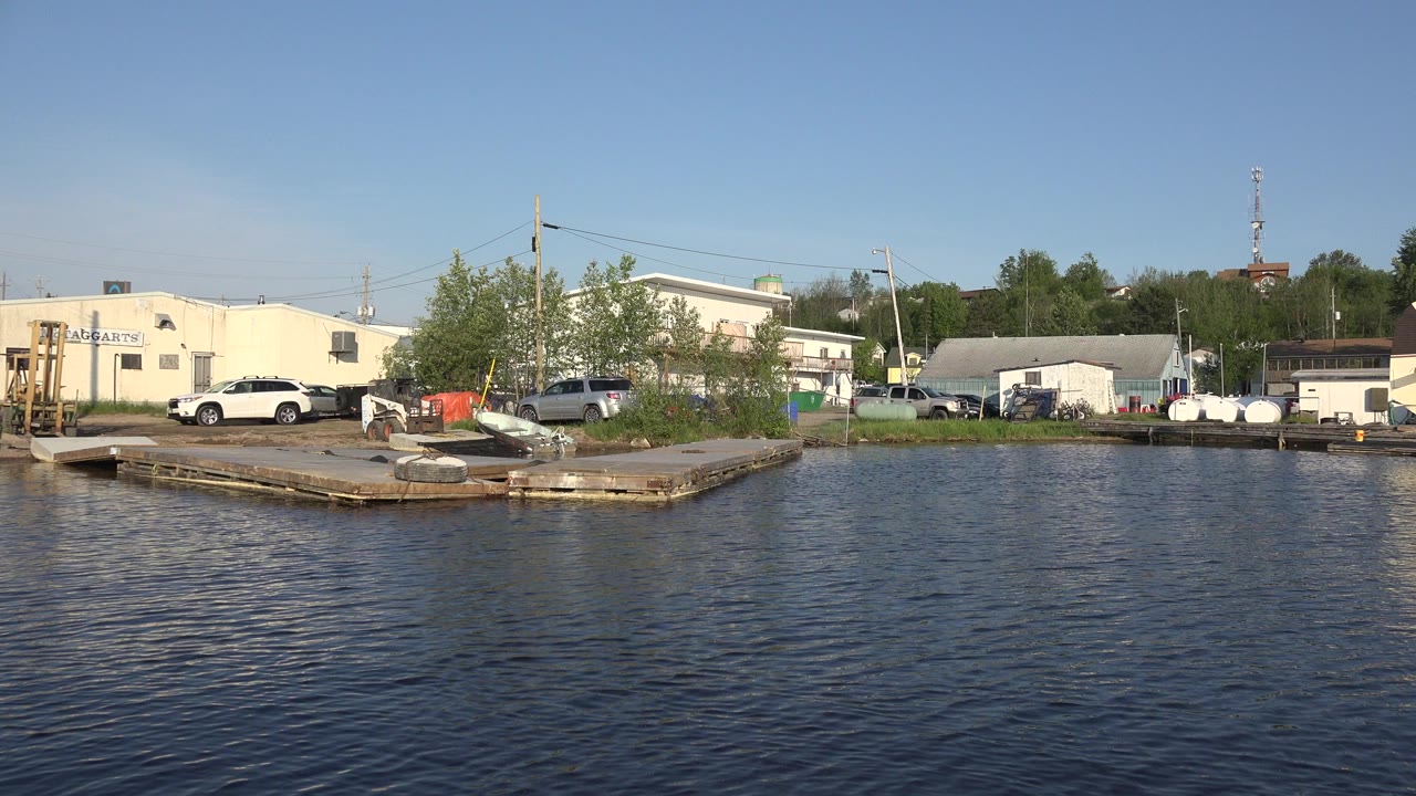 Red Lake, Canada waterfront seen across rippling water, with a small dock, light-colored buildings, parked cars, trees, utility poles, and no visible people.
