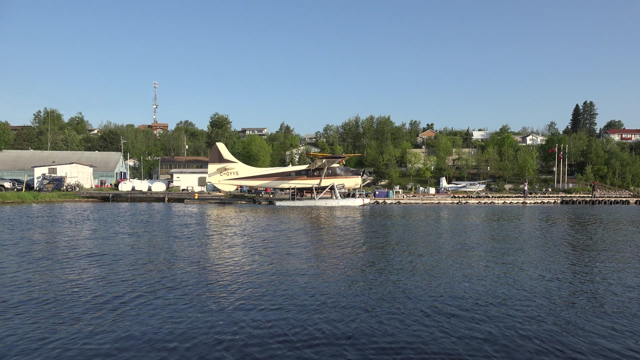 Seaplane beside shoreline buildings across calm lake water