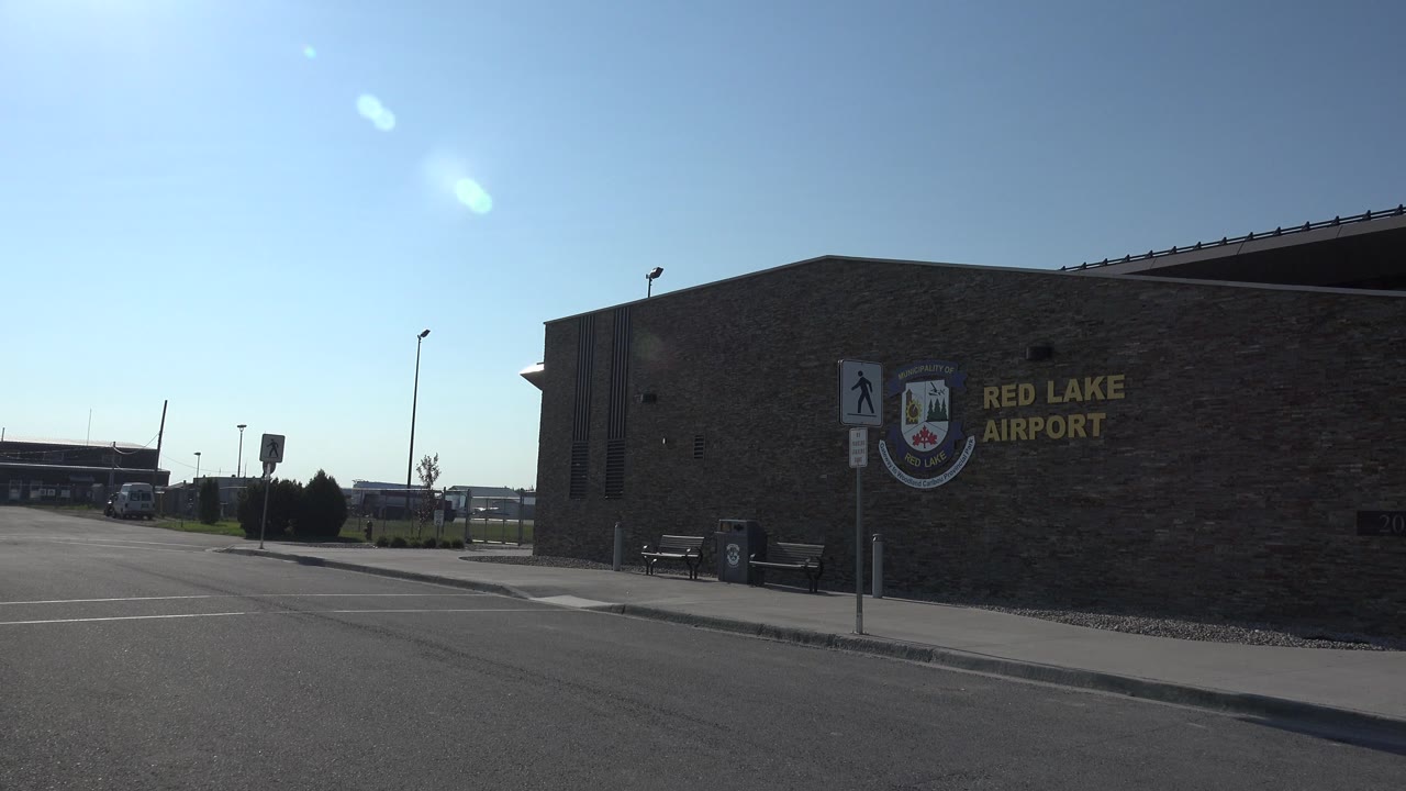 Stone airport terminal wall with Red Lake Airport lettering and sidewalk signs.