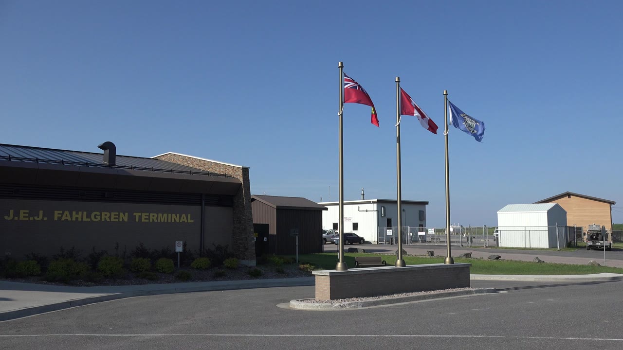 Gray terminal building beside three flagpoles under a clear blue sky.