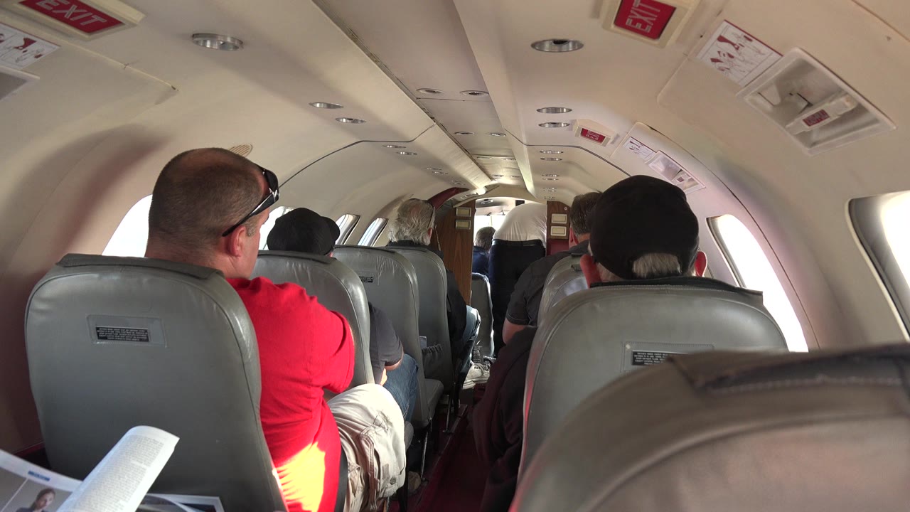 Passengers seated inside a small airplane cabin viewed from behind.