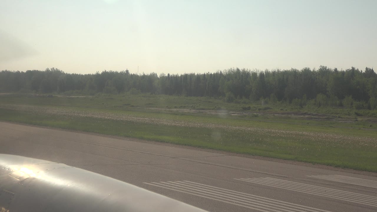 Aircraft foreground on airstrip with open field and trees