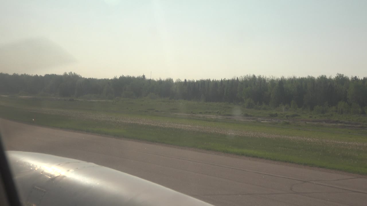 Runway and tree line seen past airplane window frame