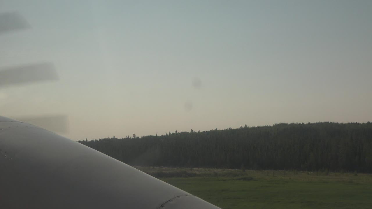 At 0:01 in Red Lake, Canada, the aircraft foreground sits diagonally across the lower frame as propeller blur appears against the sky and a dark forested horizon remains behind it, with no visible people.