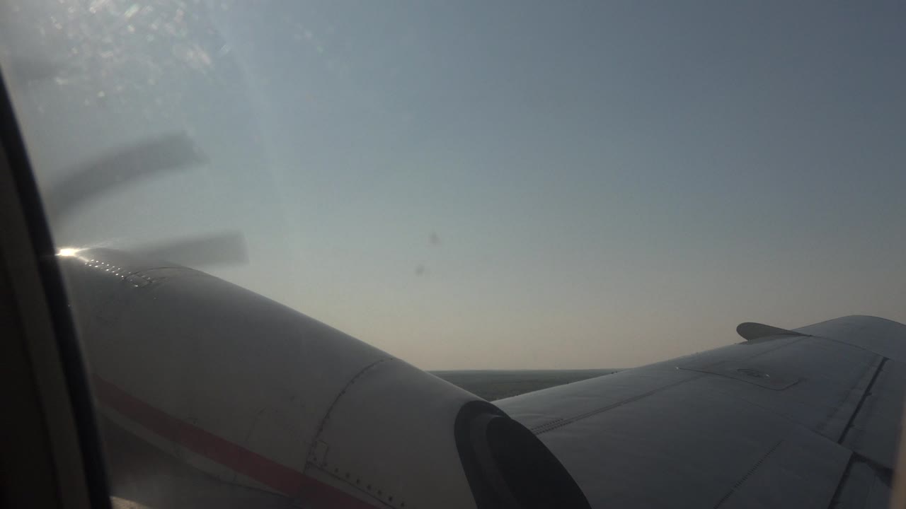 Airplane wing seen through a window above forest and water.