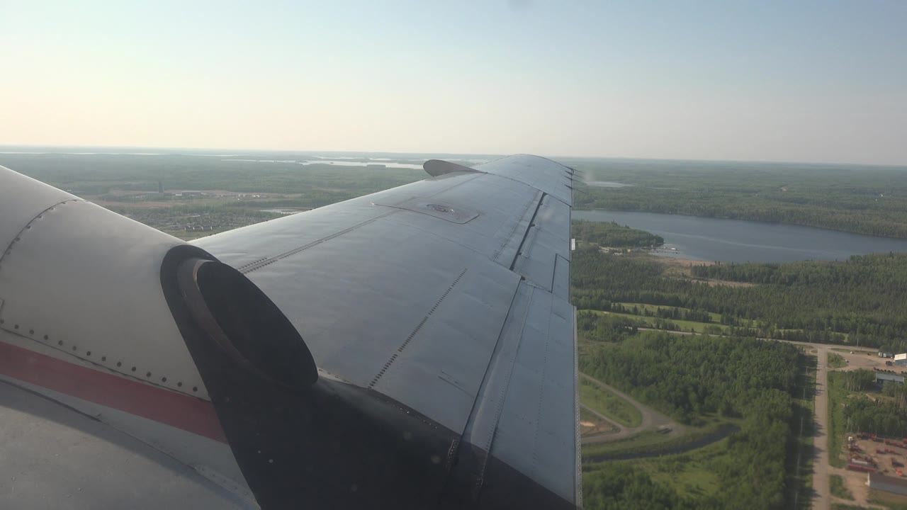 Aircraft wing over lake shoreline and forested land