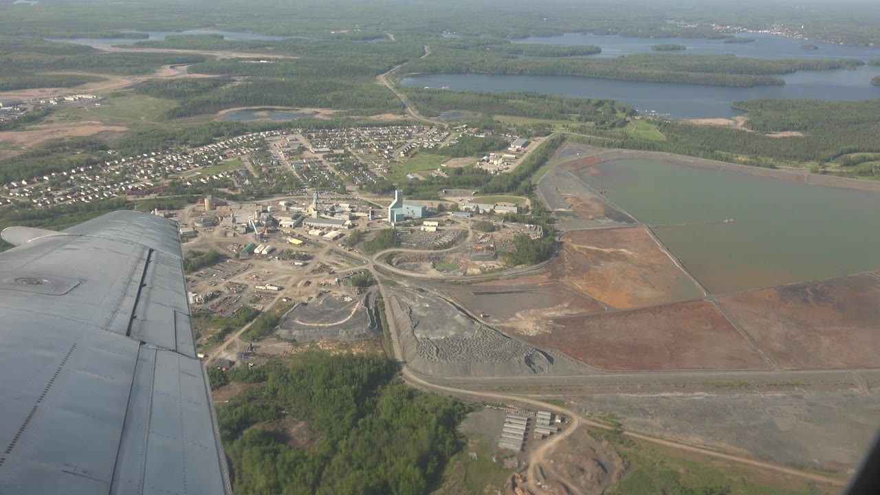 Airplane wing over forest, buildings, roads, and water.
