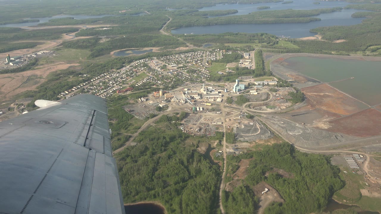 Aerial view from a plane over Red Lake, Canada, with the gray wing at lower left, a town and industrial area below, lakes beyond, and no visible people.