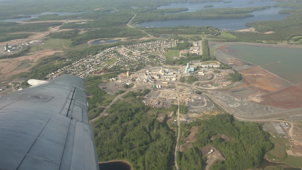A slightly later aerial view of Red Lake, Canada, shows the plane wing lower left, a clustered town area below, pale roads, green forest, and no visible people.