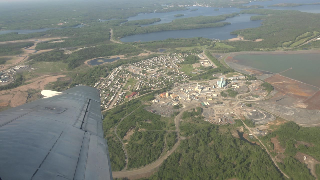 Airplane wing above forest, lakes, roads, homes, and industrial buildings.