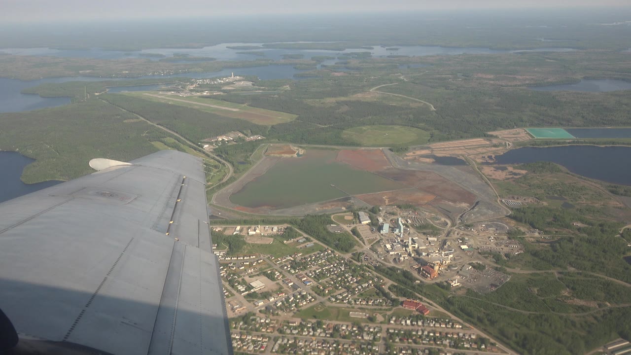 Airplane wing over forest, lakes, roads, and buildings.