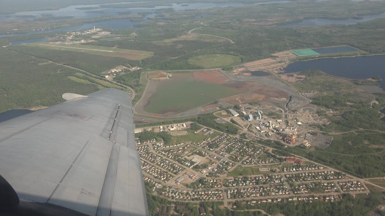 Airplane wing above a town, forest, and lakes.