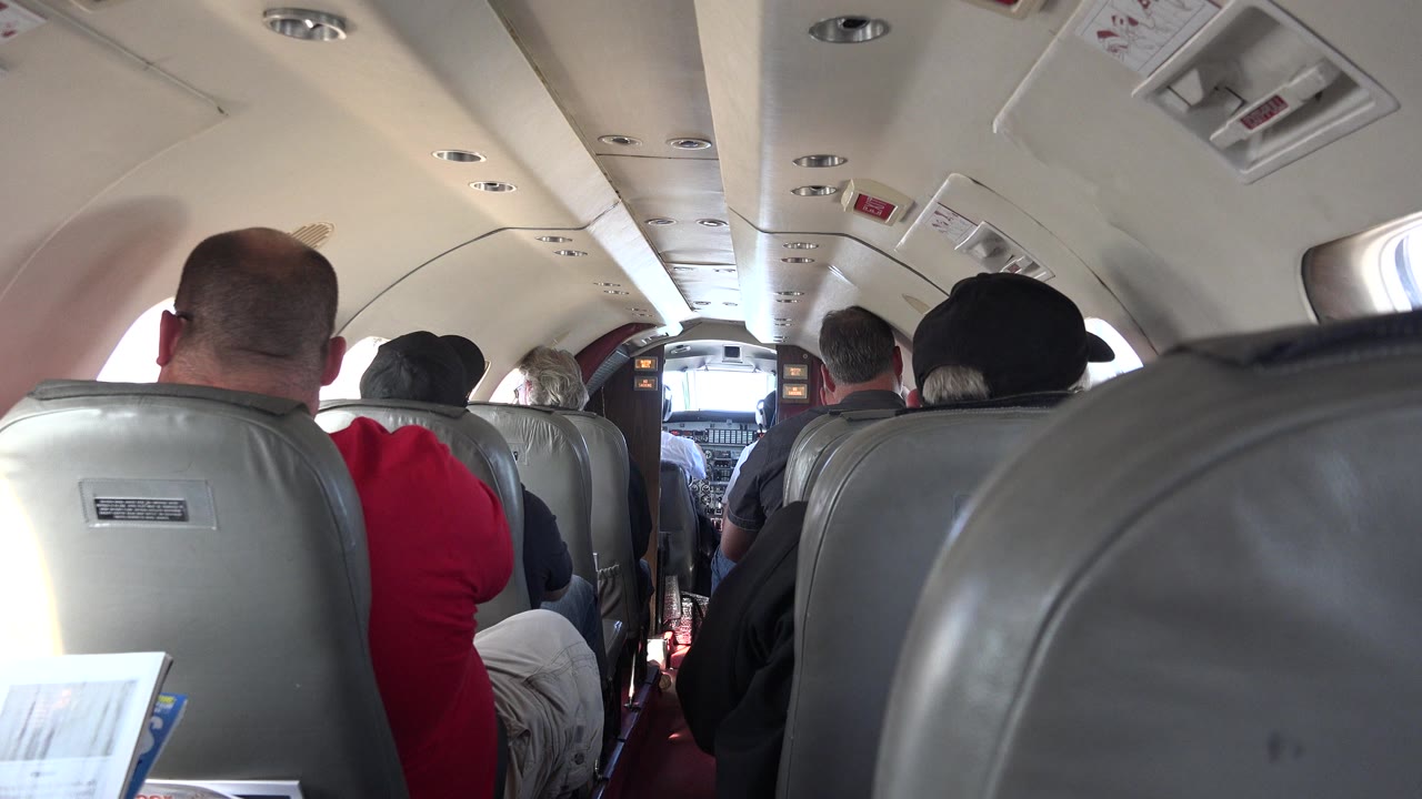 Small aircraft cabin viewed from behind passengers toward cockpit.