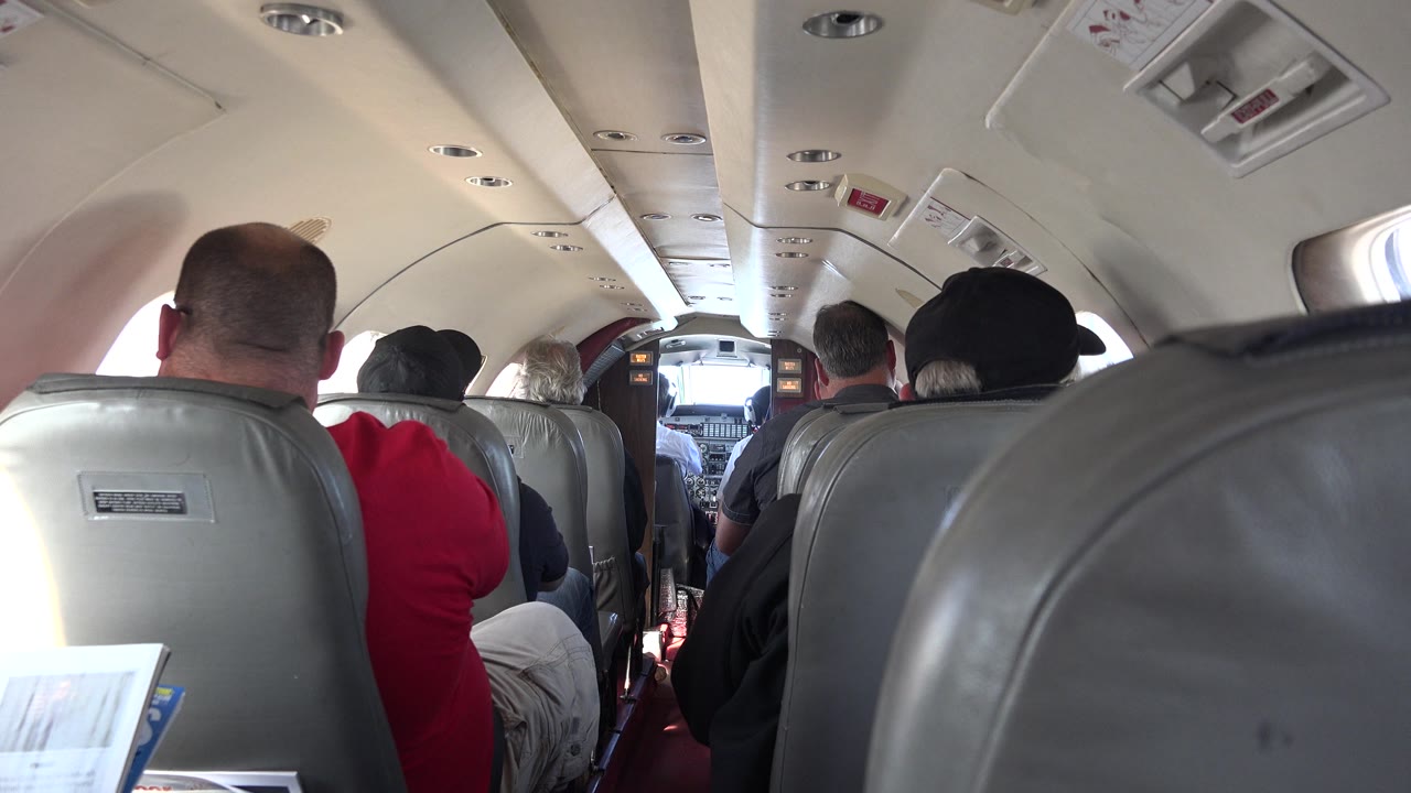 Cabin aisle view with seatbacks, passengers, and cockpit ahead.