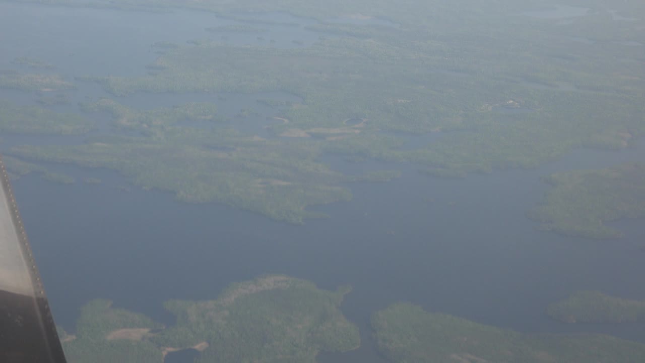Opening frame from an airplane window over Red Lake, Canada, showing blue water, green land masses, haze, and no visible people.