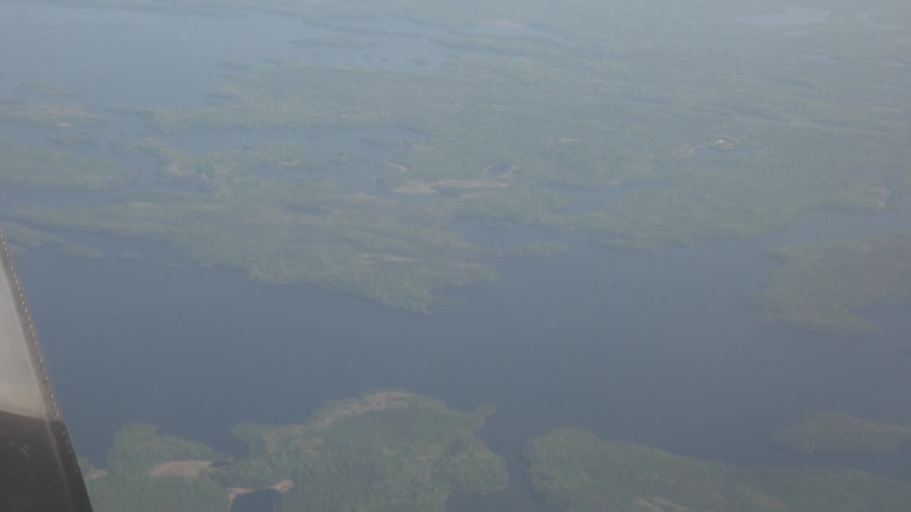 Airplane-window frame over Red Lake, Canada, with a dark aircraft edge at left, broad blue water below, green shorelines, and no visible people.