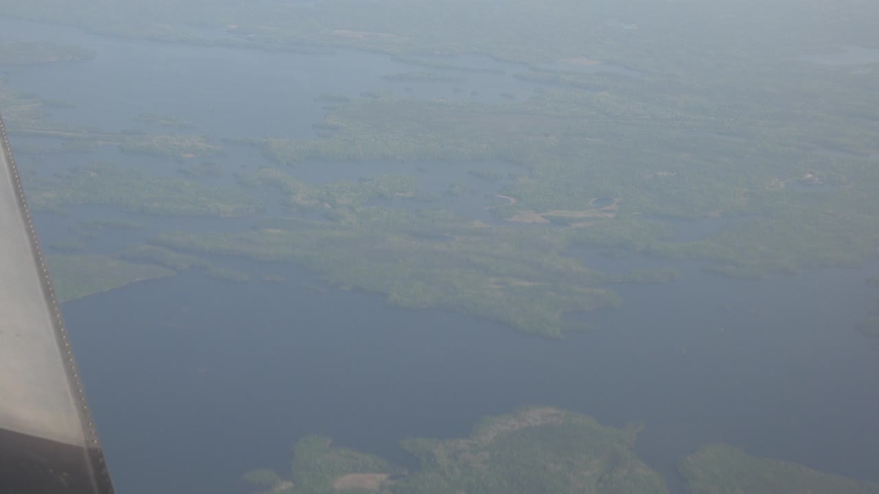 Opening view from above Red Lake, Canada, with an airplane wing at the left edge, dark water below, green shoreline in the distance, and no visible people.